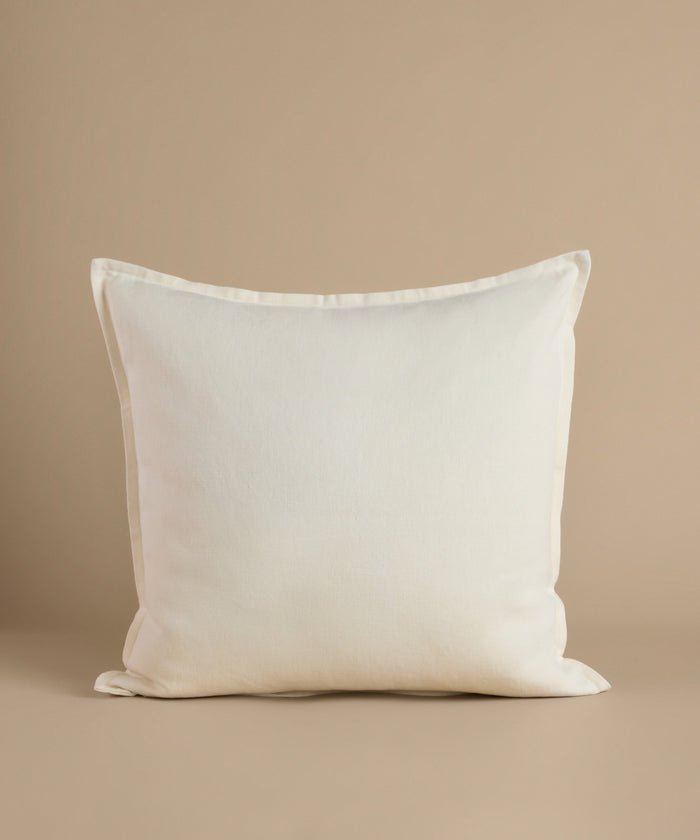 A white square pillow against a beige background.