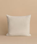 The Alpaca Basketweave Pillow, a square white accent, is handmade in Peru and sits upright on a beige surface with a matching beige background for an elegant touch.