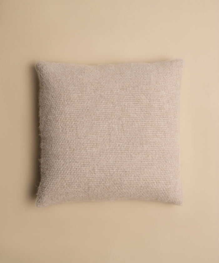The Alpaca Basketweave Pillow, featuring a square, textured design, is centered on a matching beige background for a soft, minimalistic appearance.