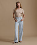 Woman wearing a beige t-shirt and light blue jeans against a brown background