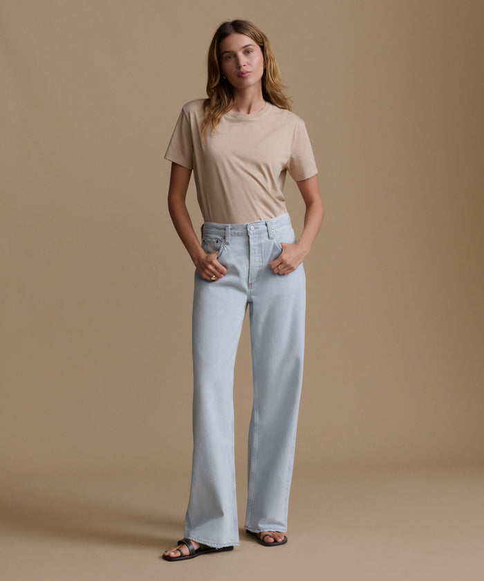 Woman wearing a beige t-shirt and light blue jeans against a brown background