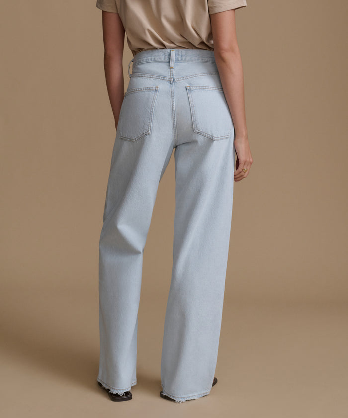 Person wearing light blue jeans on a beige background