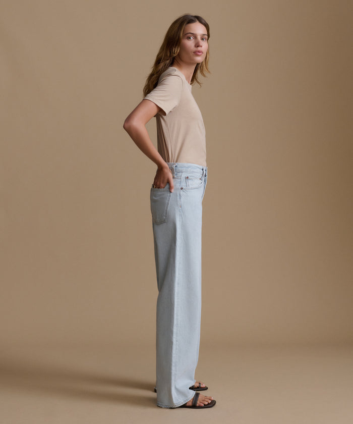 Woman wearing a beige t-shirt and light blue jeans against a brown background