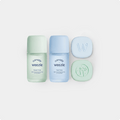 Three Weezie skincare items arranged on a light gray background: a mint green Travel Time bottle, a light blue Tub Time bottle, and two matching round bars, one embossed with a W and the other with a face outline.
