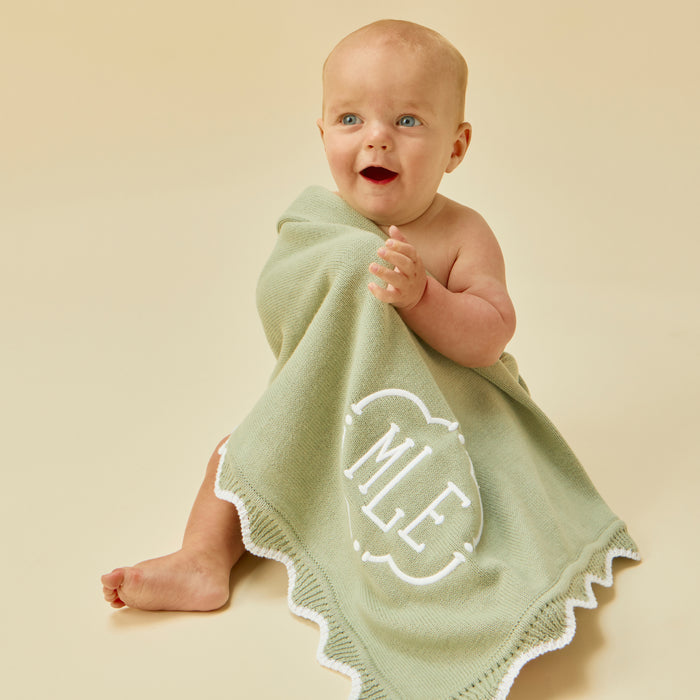 Smiling baby wrapped in a matcha green blanket with white scalloped edges and an MLE monogram.