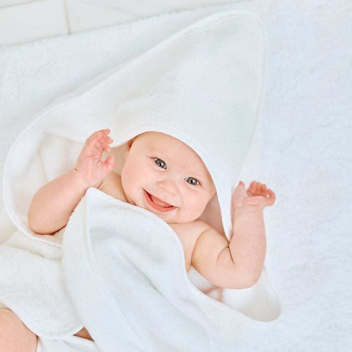 A smiling baby wrapped in a white hooded towel, lying on a soft white blanket.