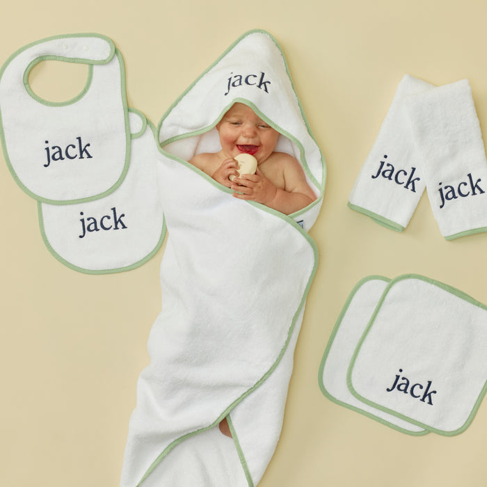 Baby in hooded towel with matching bibs, burp cloths, and washcloths featuring green trim and jack embroidery.