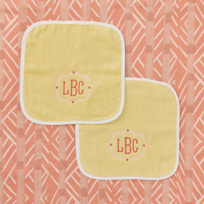 Two buttercup yellow baby washcloths with white piping and LBC monograms.