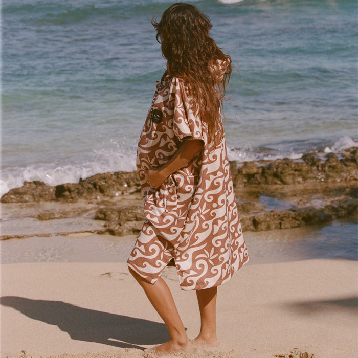 Changing poncho, recycled materials, patterned design, on sandy beach with ocean waves.