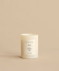A white Basil Glass Candle labeled jenni kayne sits on a beige surface. Hand-poured in Los Angeles, it features notes of neroli, green herbs, and jasmine—a blend from Oprah’s Favorite Things.