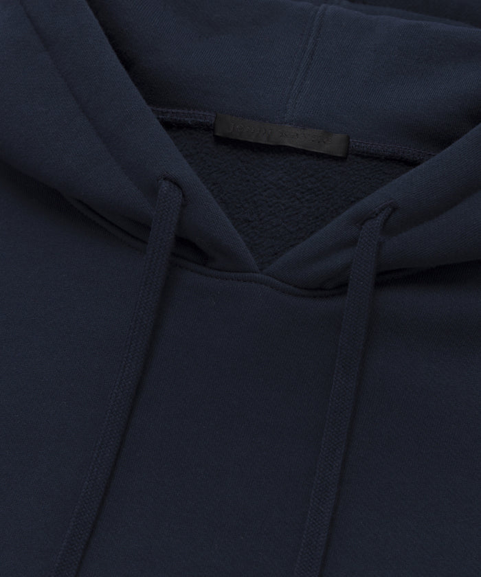 Close-up of the Bay Hoodie in dark navy blue, made from soft brushed fleece, highlighting the hood, drawstrings, collar, and a blank black tag.