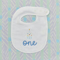 Detail of the embroidered cupcake and blue 'one' on a white birthday bib.