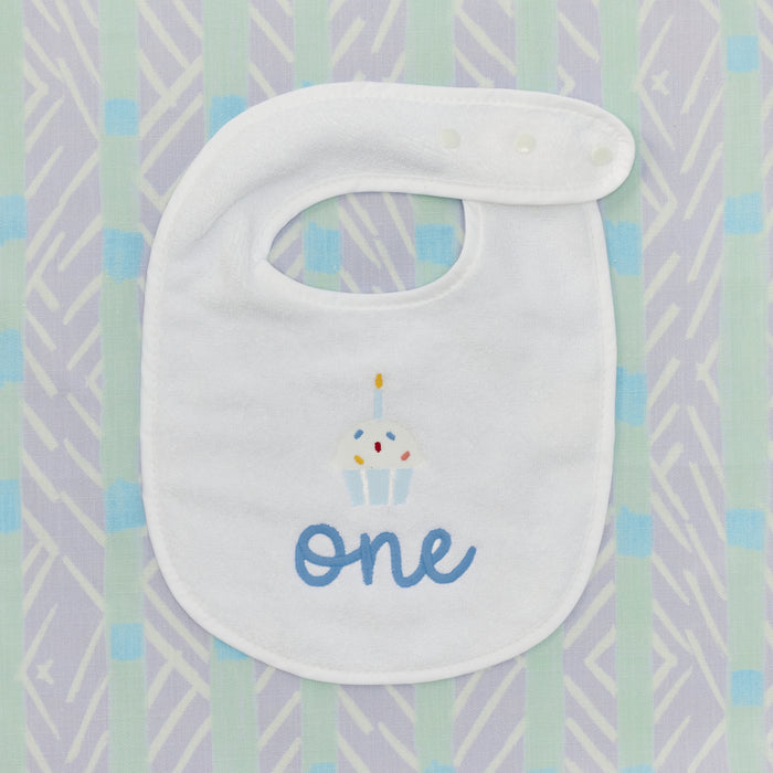 Detail of the embroidered cupcake and blue 'one' on a white birthday bib.