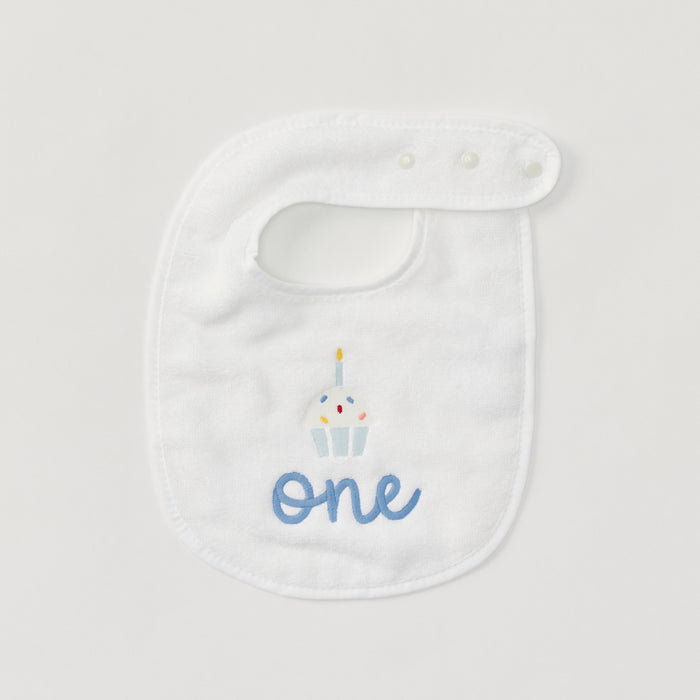 Detail of the embroidered cupcake and blue 'one' on a white birthday bib.