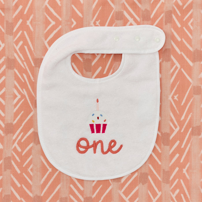 Detail of the embroidered cupcake and pink 'one' on a white birthday bib.