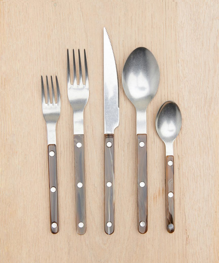 Five pieces from the Bistro Vintage Finish Cutlery Set—a small fork, large fork, knife, large spoon, and small spoon—are arranged side by side. Each has a metal top and brown handle with three silver rivets.