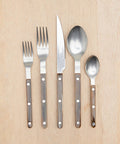 Five pieces from the Bistro Vintage Finish Cutlery Set—a small fork, large fork, knife, large spoon, and small spoon—are arranged side by side. Each has a metal top and brown handle with three silver rivets.