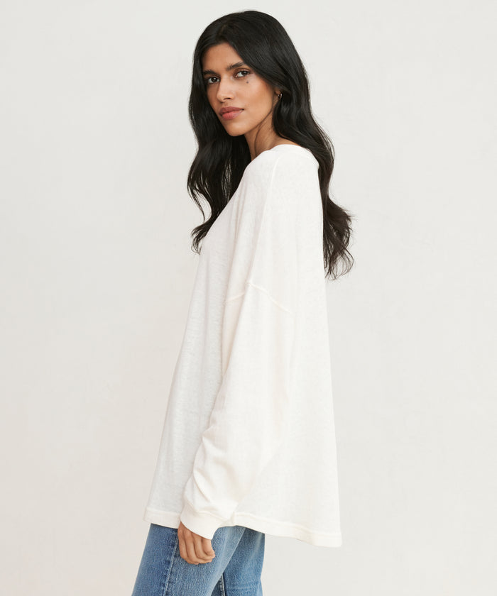 A woman with long dark hair models the Boyfriend Long-Sleeve Tee with blue jeans, standing sideways and looking at the camera against a plain light background.
