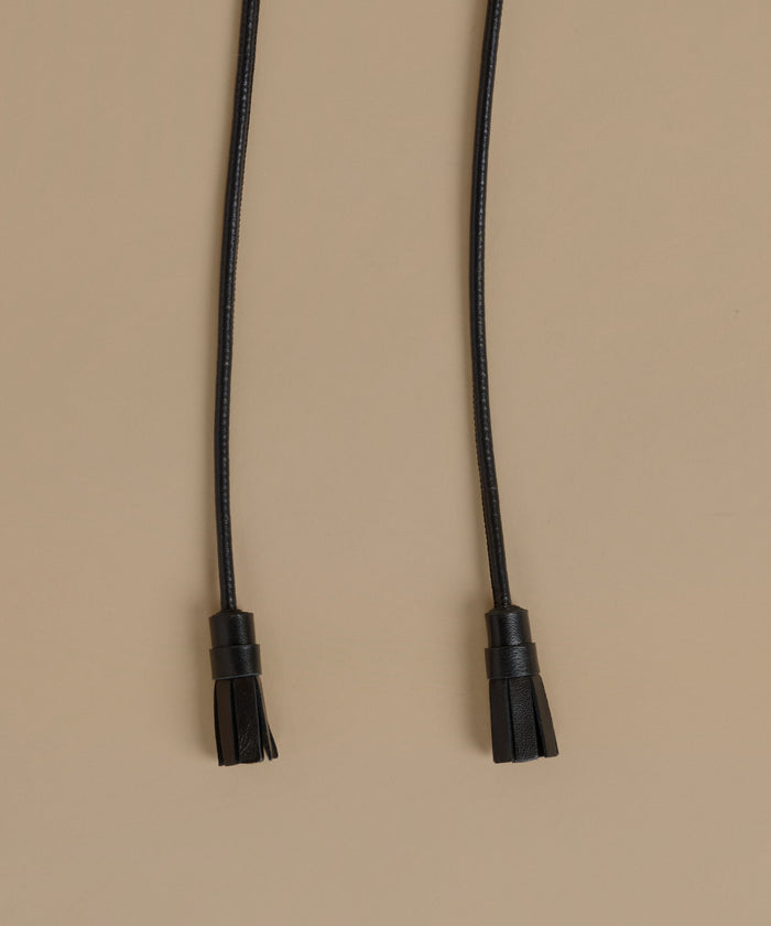 A black leather cord belt with tassel ends, laid flat on a solid beige background.