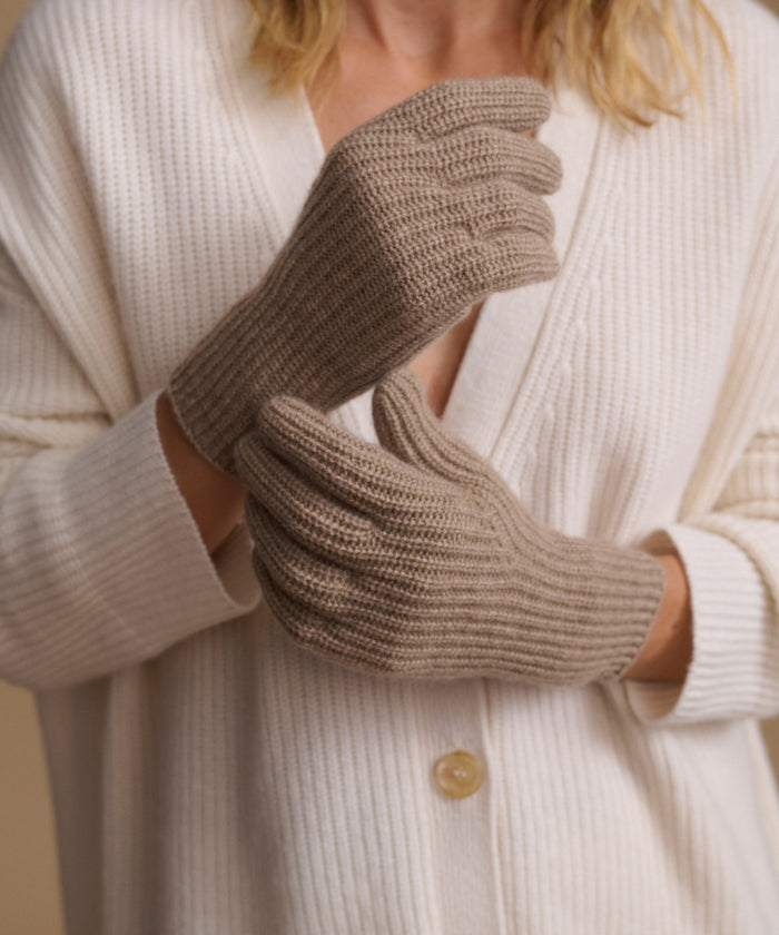 A close-up of a person wearing beige ribbed knit gloves over a cream-colored cardigan.