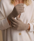 A close-up of a person wearing beige ribbed knit gloves over a cream-colored cardigan.