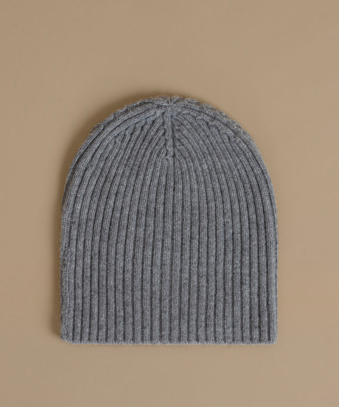 A gray ribbed knit beanie hat photographed flat against a solid beige background.