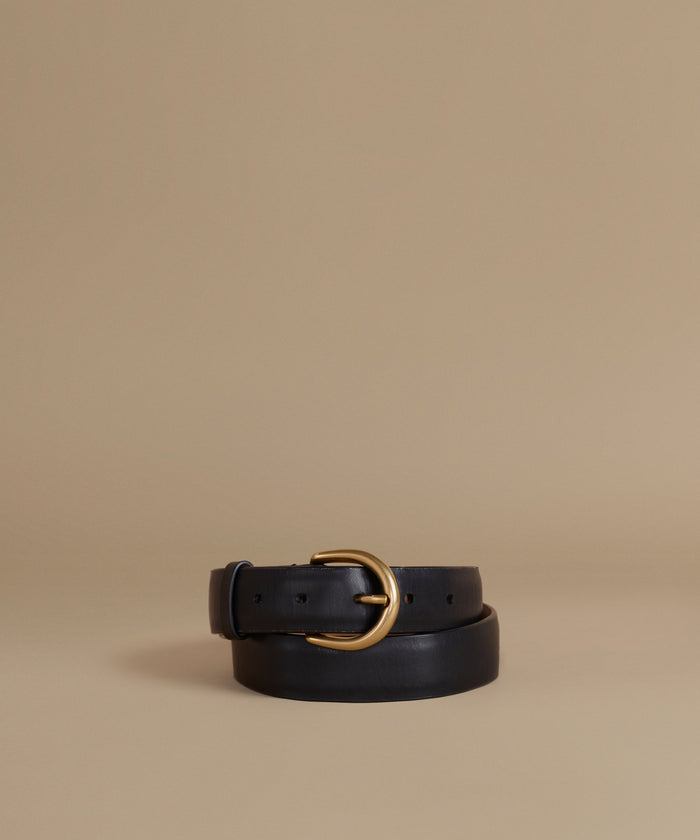 A black leather belt with a polished gold-tone metal buckle, neatly coiled on a warm beige studio background.