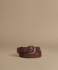 A dark brown leather belt with a silver-tone metal buckle, neatly coiled on a solid beige background.