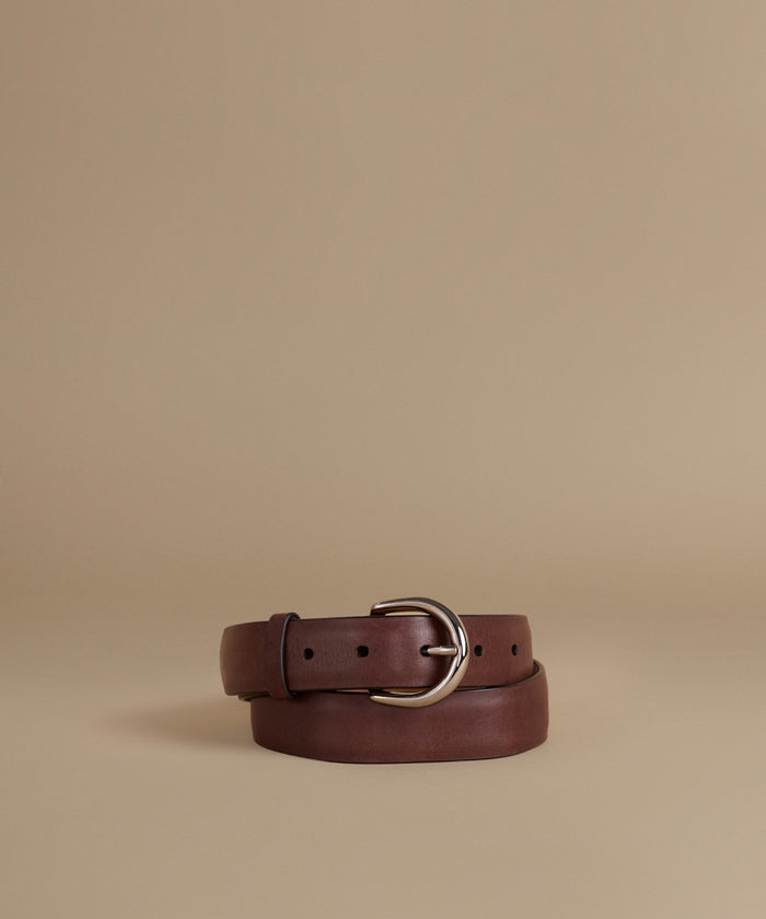 A dark brown leather belt with a silver-tone metal buckle, neatly coiled on a solid beige background.