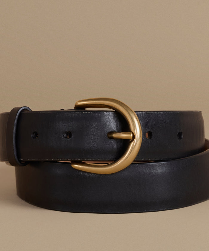 A black leather belt with a polished gold-tone metal buckle, coiled on a neutral beige background.