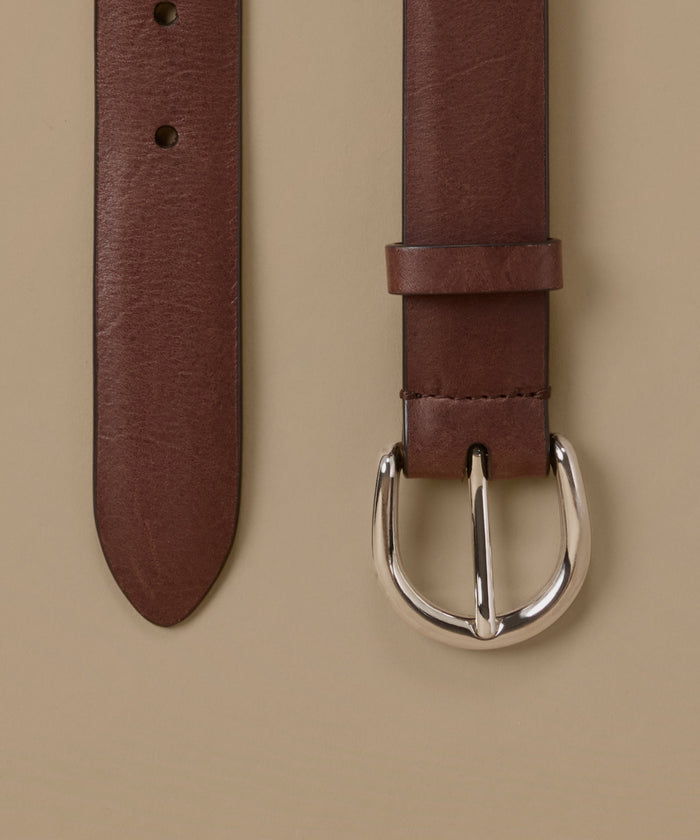 A close-up of a brown leather belt showing the strap end and buckle against a solid beige background.