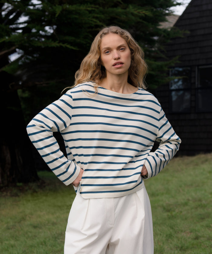 Woman wearing a striped shirt and white pants standing outdoors.