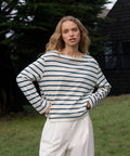 Woman wearing a striped shirt and white pants standing outdoors.