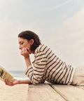 Woman in striped shirt reading a book on a sandy beach.