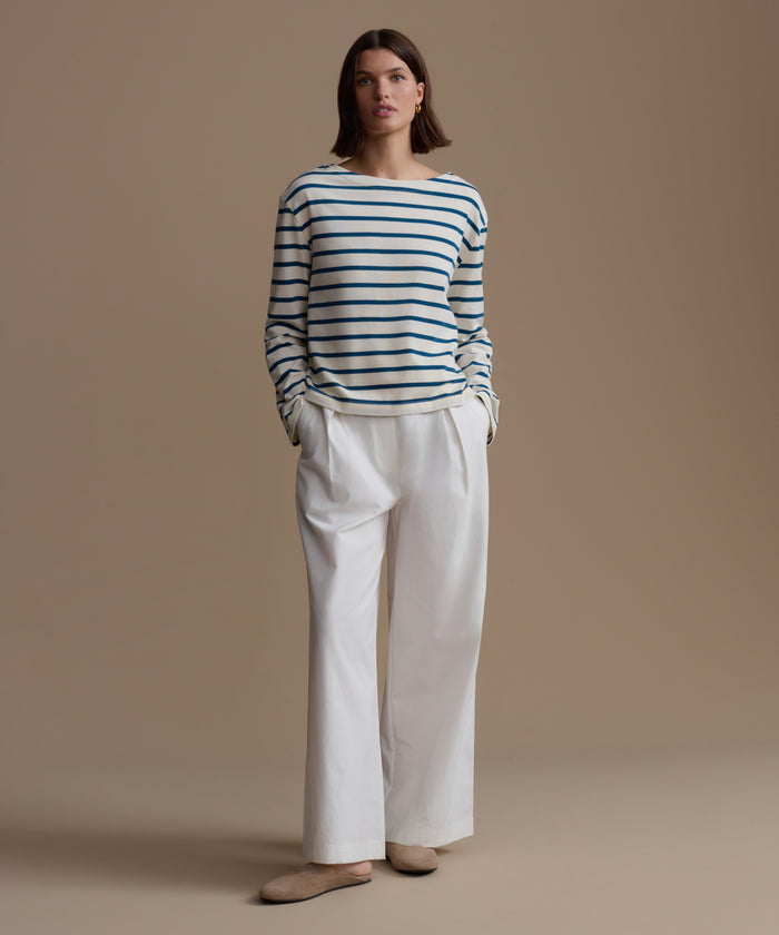 Woman wearing a striped shirt and white pants against a beige background