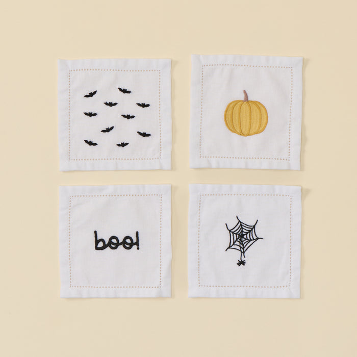 Four white cocktail napkins with Halloween embroidery: bats, pumpkin, boo, and spiderweb.