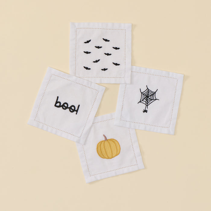 Four white cocktail napkins with Halloween embroidery: bats, pumpkin, boo, and spiderweb.
