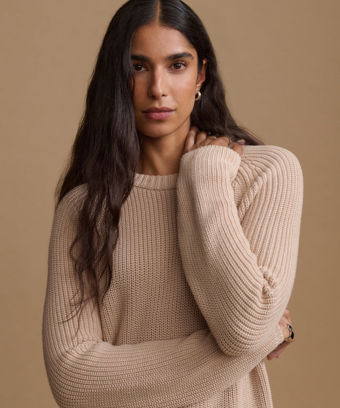 A woman wearing a beige ribbed knit sweater, posed against a solid beige background.
