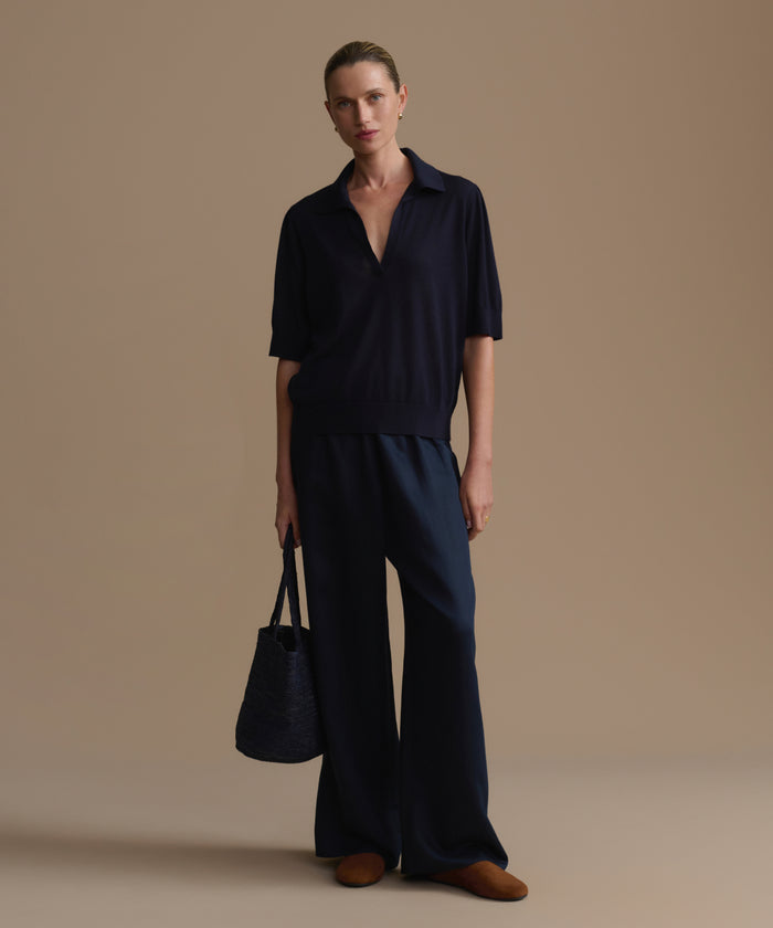 Woman wearing a navy outfit holding a black handbag against a beige background