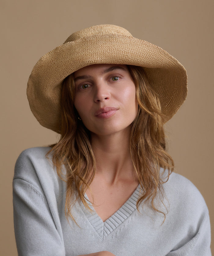 Woman wearing a beige straw hat against a beige background