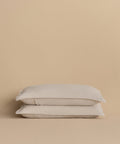 Two Dusk Linen Pillow Shams, in light beige and crafted from lightweight linen, are stacked neatly against a matching beige background.