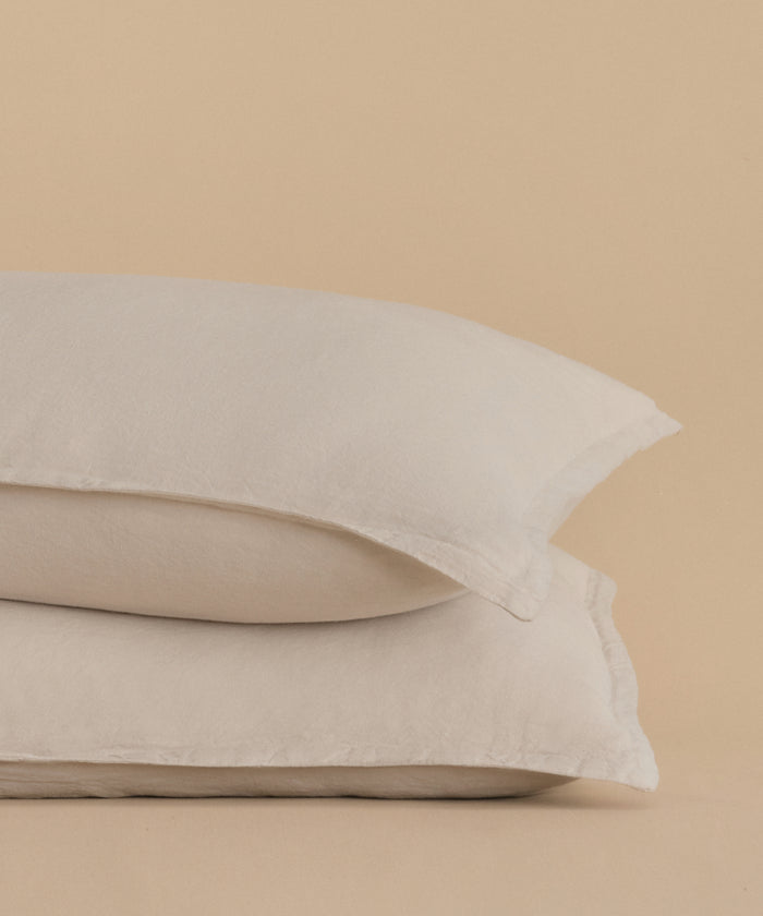 Two white Dusk Linen Pillow Shams, sold as a set of 2 and made in Portugal, are stacked atop each other against a beige background.