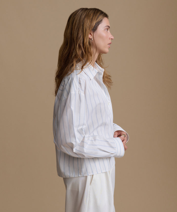 Woman wearing a blue and white stripe shirt with white pants against a beige background.