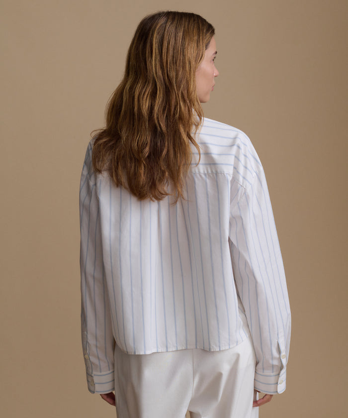 Woman wearing a blue and white stripe shirt with white pants against a beige background.