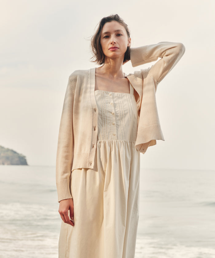 Woman wearing an ivory cardigan with an ivory dress at the beach.