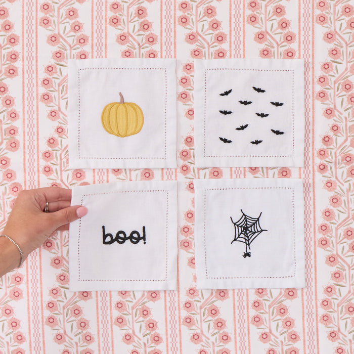 four white Halloween embroidered cocktail napkins, featuring pumpkin, bats, "boo" and spiderweb embroidery.