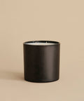 The Extra Large Topanga Glass Candle features a sleek black cylindrical design with three wicks. Hand-poured in Los Angeles, it is displayed on a beige surface with a matching beige background.