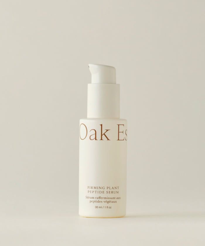 A white pump bottle labeled “Firming Plant Peptide Serum” stands upright against a plain light background; the minimal beige text highlights its powerful plant peptide formula known as a collagen booster.