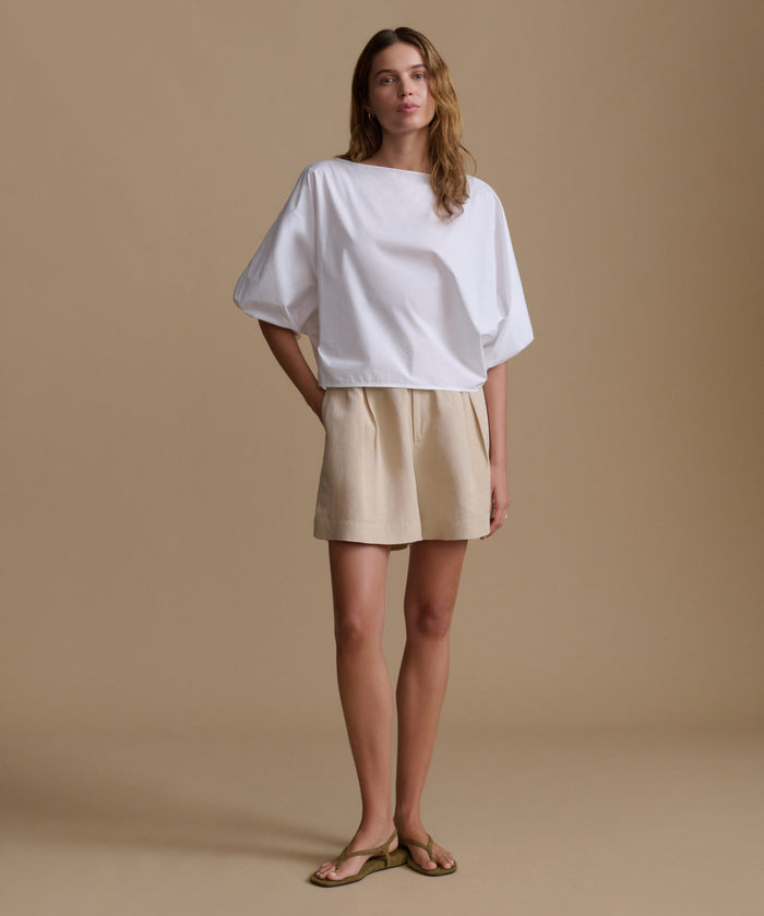 Woman wearing a white blouse and beige shorts against a beige background.