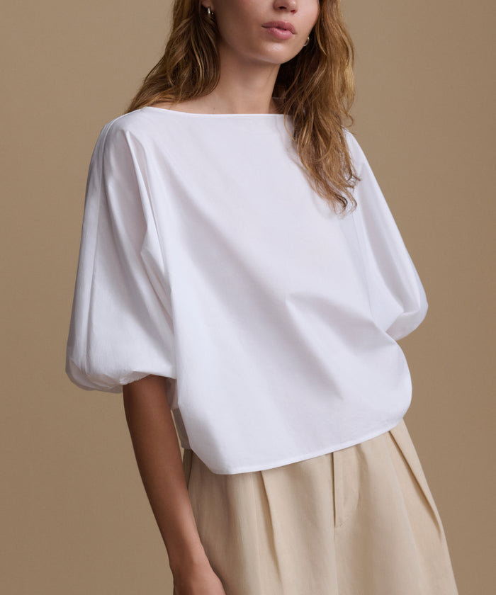 Woman wearing a white blouse and beige shorts against a beige background.